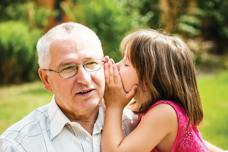 grandfather with granddaughter speaking into ear - hearing health