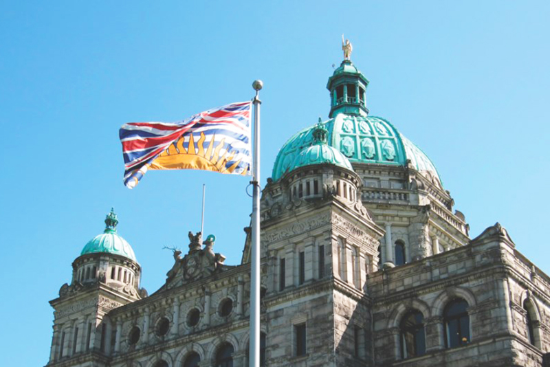BC Politics - BC Legislature Building with BC Flag waving in front.