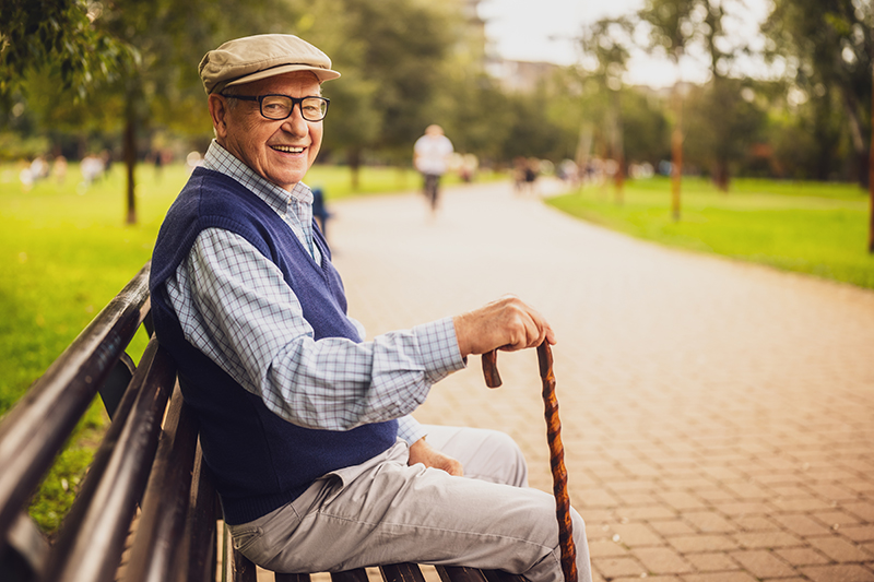 Support for older men - a lonely, friendly senior man in park. He is sitting on bench and enjoying autumn day.